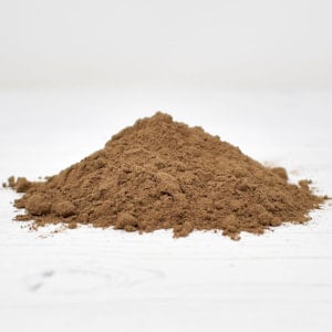 Garam masala spice in a conical mound with a granular, mid-brown texture set against a white slatted background.