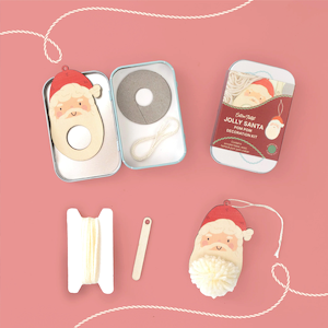 Cotton Twist Jolly Santa pom pom decoration kit, showing a metal tin, wooden Santa base, white yarn, and a finished ornament.