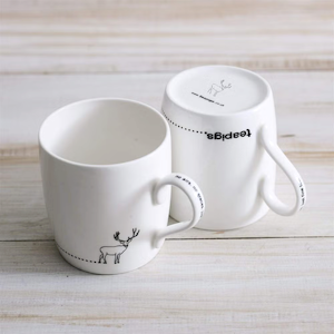Two white fine bone china Teapigs stag mugs, one upright, one inverted on wood.